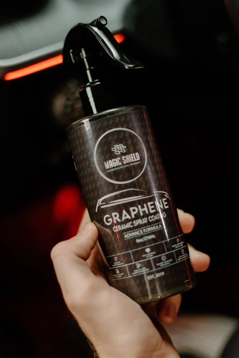 Magic Shield Graphene Ceramic Spray Coating 9oz bottle held beside a vehicle
